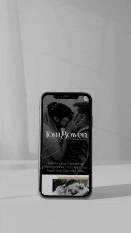 A smartphone displaying the website for "Tom Bowen Photography," featuring a black-and-white image of a couple embracing, with text stating, “A Birmingham Wedding Photographer That Helps You Have Your Day, Your Way.” The minimalist, elegant design emphasises a personalized, intimate wedding photography experience.