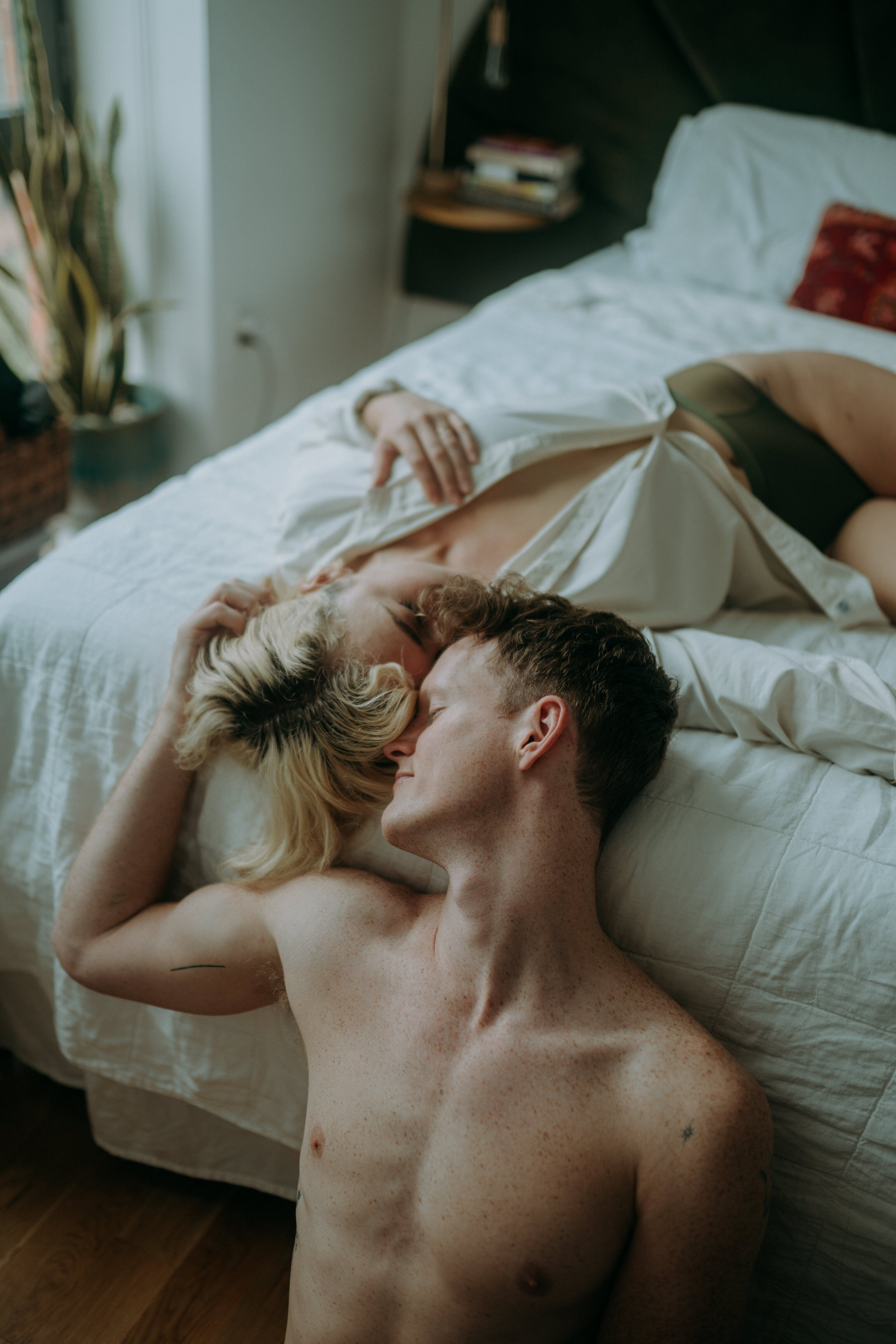 Couple lying on a bed and floor, embracing intimately in a sunlit room