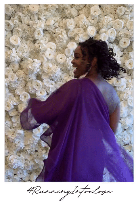 woman holding her purple dress for a boomerangs front of a flower wall