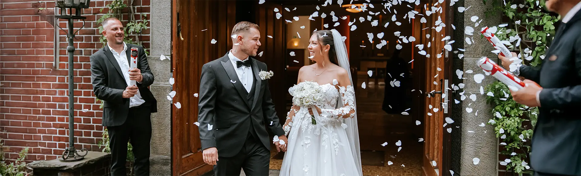 Konfettiregen beim Auszug: Braut und Bräutigam lächeln und treten gemeinsam aus dem Portal, als natürliche hochzeitsfotografie mit emotionalen hochzeitsbildern