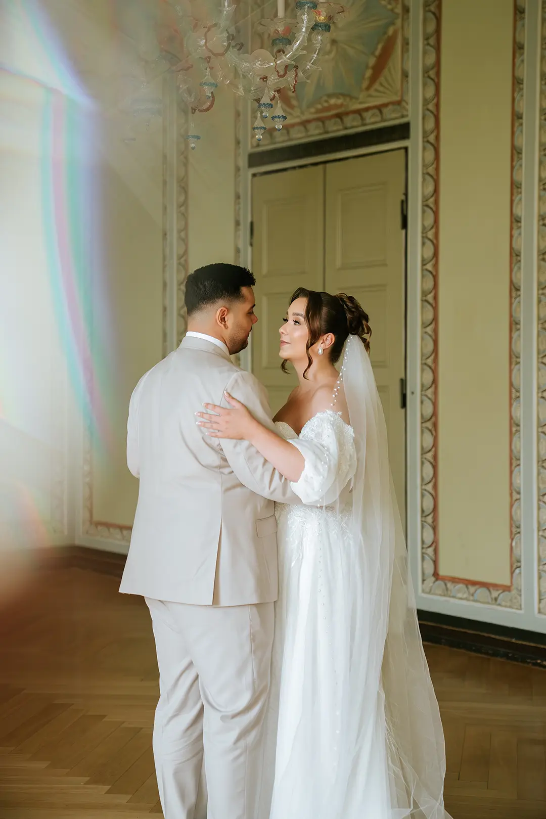 Braut und Bräutigam umarmen sich sanft im historischen Saal, zarte Lichtreflexe und Stuckrahmen – ein Moment voller Nähe, festgehalten als emotionale Hochzeitsbilder von einem professionellen Fotografen