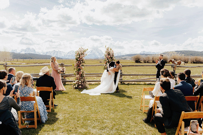 photo of bride and groom at their wedding ceremony with horses running behind them in the distance