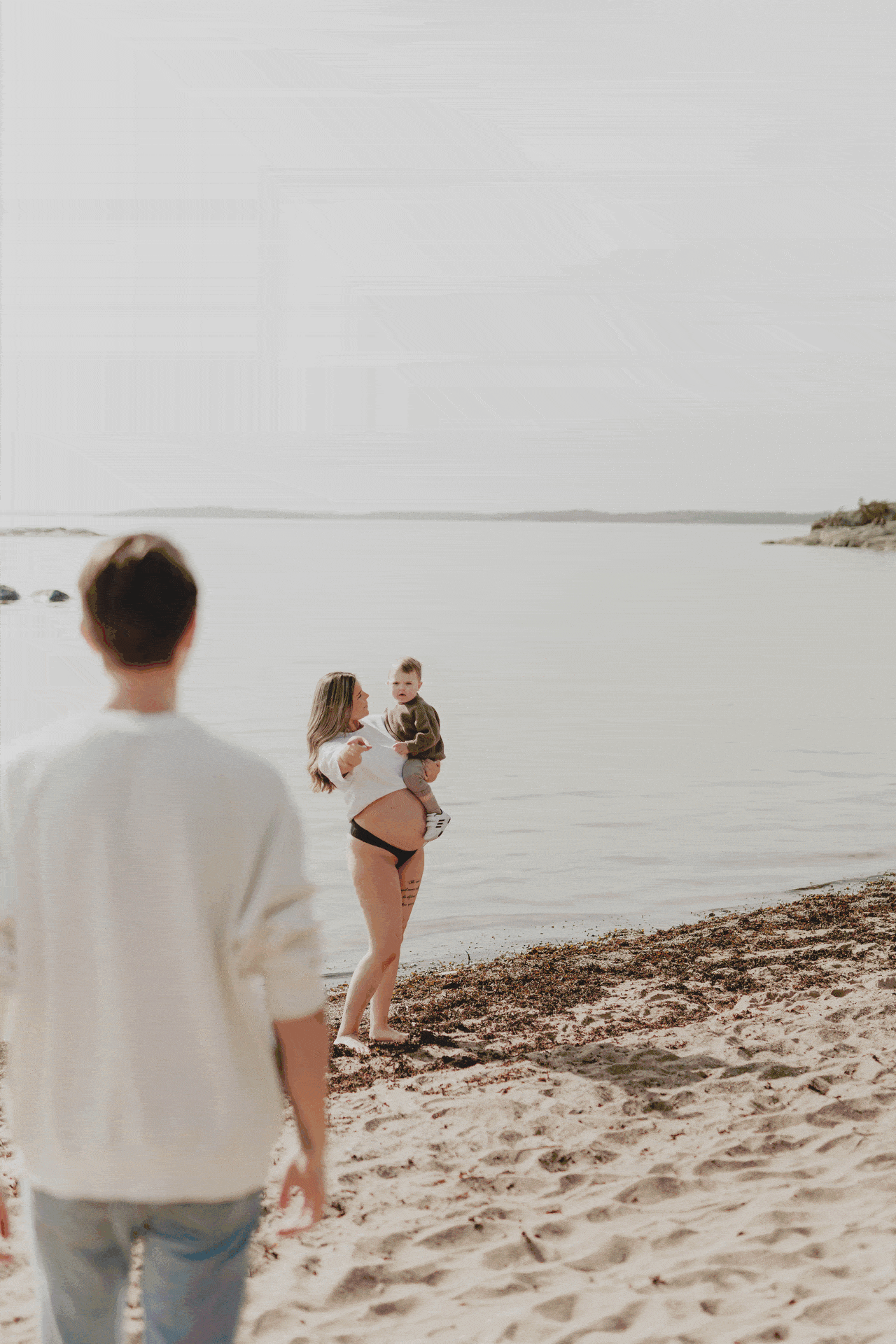 En gif-fil på en gravid kvinna tillsammans med sin partner hållandes sin son på en strand under en gravidfotografering i Stockholm