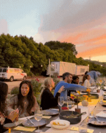 Guests enjoying a farm-to-table dinner outdoors around a table as the sun sets, sharing food and conversation at a Farm Dinner LA event