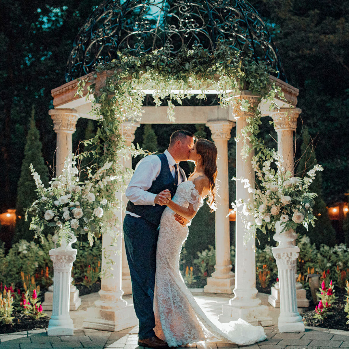 Hamilton Manor Wedding | Bride and groom kissing under gazebo with ivy, flowers, and twinkle lights at night | Hamilton Township, New Jersey
