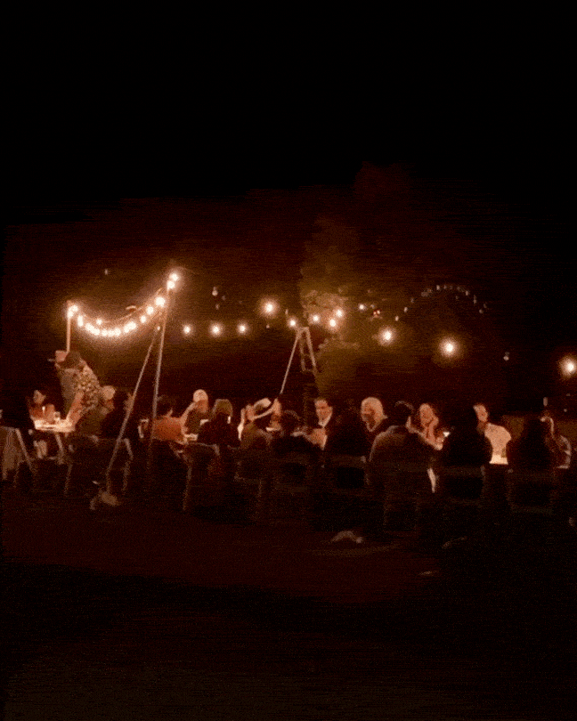 Guests enjoying a farm-to-table dinner outdoors around a table at night, sharing food and conversation at a Farm Dinner LA event