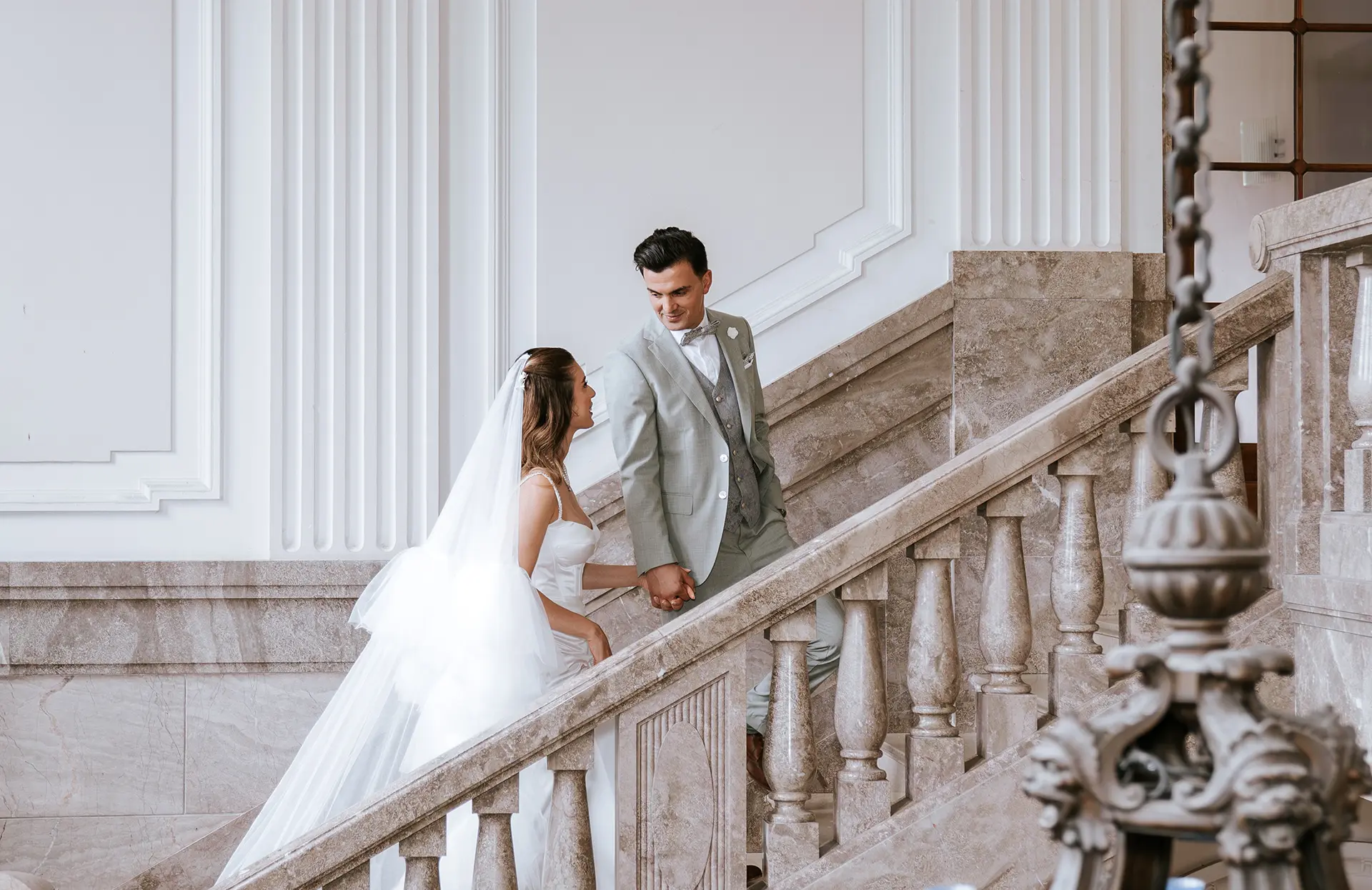 Hand in Hand steigen Braut und Bräutigam die marmorierte Treppe eines eleganten Saals hinauf; klassische hochzeitsfotos, fine art hochzeitsfotografie und hochzeitsfotografie mit stil