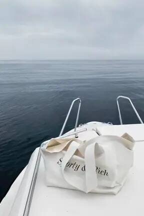Linen tote bag labeled 'Sporty and Rich' placed on a luxury yacht deck overlooking a serene blue sea – minimalist lifestyle scene by Ana Gicel