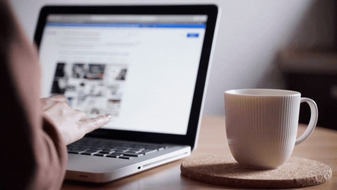 Someone typing on a laptop with a cup of coffee beside them