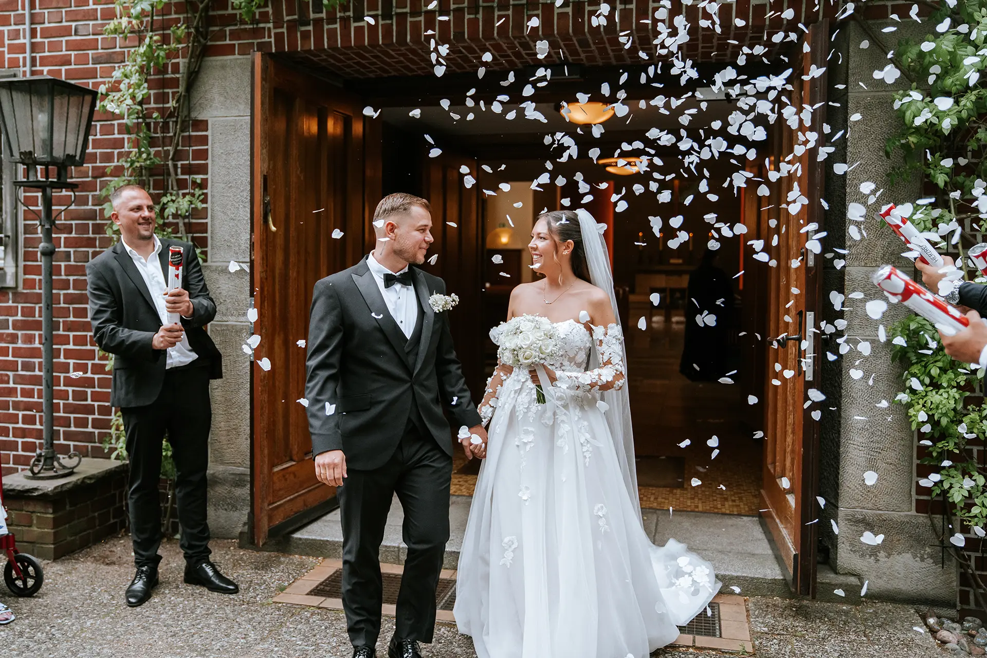 Konfettiregen beim Auszug: Braut und Bräutigam lächeln und treten gemeinsam aus dem Portal, als natürliche hochzeitsfotografie mit emotionalen hochzeitsbildern