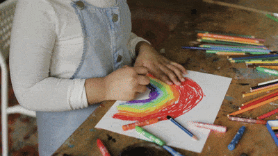 A video of a child drawing a rainbow with crayons and moving her crayons off her drawing