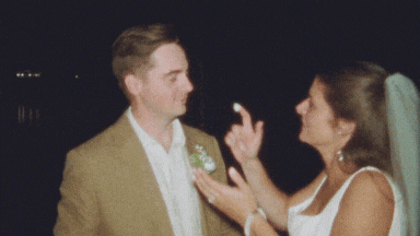 Super 8 film still of a bride and groom laughing and feeding each other cake at night — a nostalgic moment captured by a vintage wedding videographer