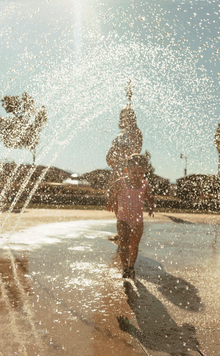 gif of a toddler in a pink swimsuit running through a sprinkler.