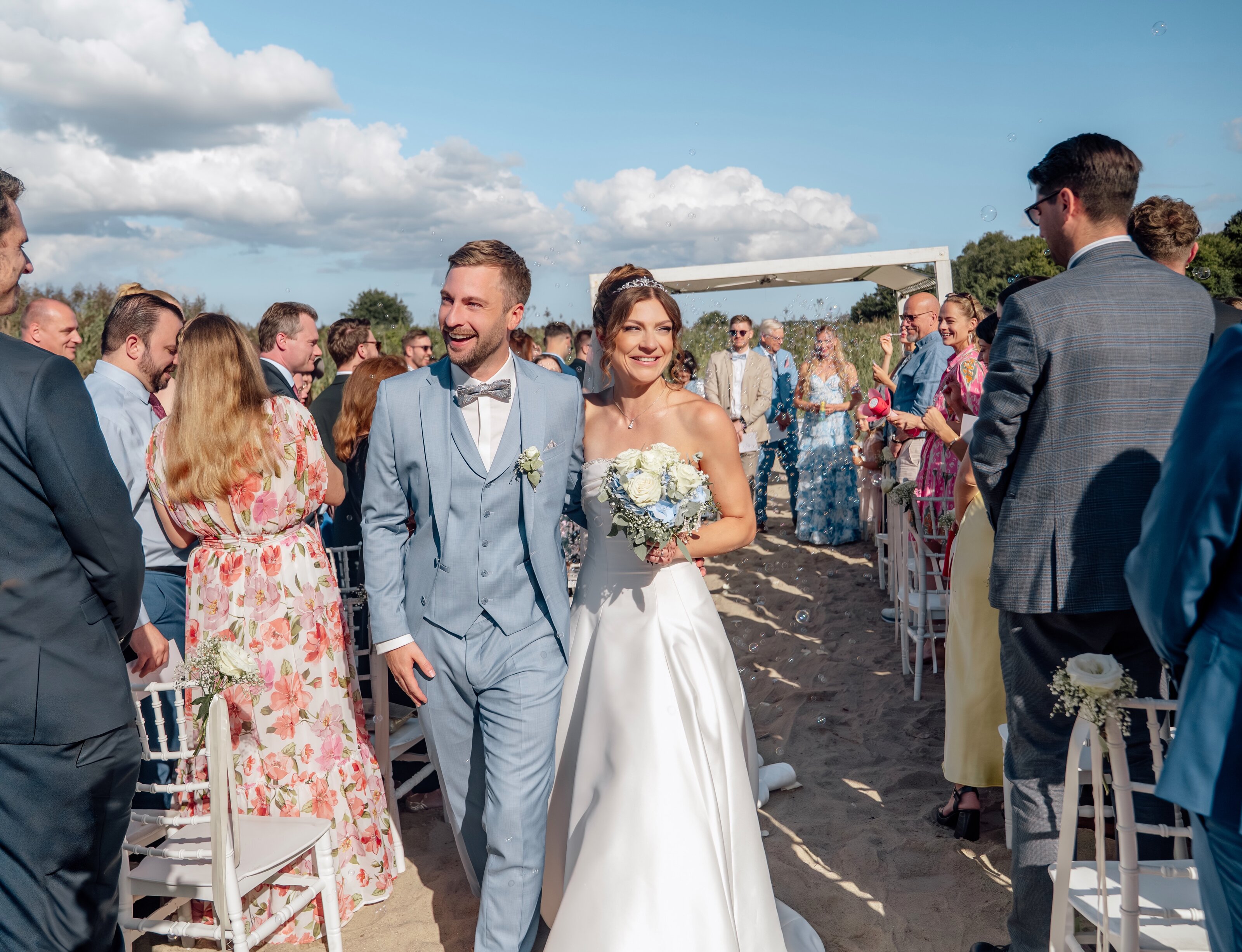 Beim Sektempfang unter dem Sonnenschirm küssen sich Braut und Bräutigam, Gäste stoßen mit Sekt an; moderne hochzeitsfotografie fängt emotionale hochzeitsbilder und klassische hochzeitsfotos ein.