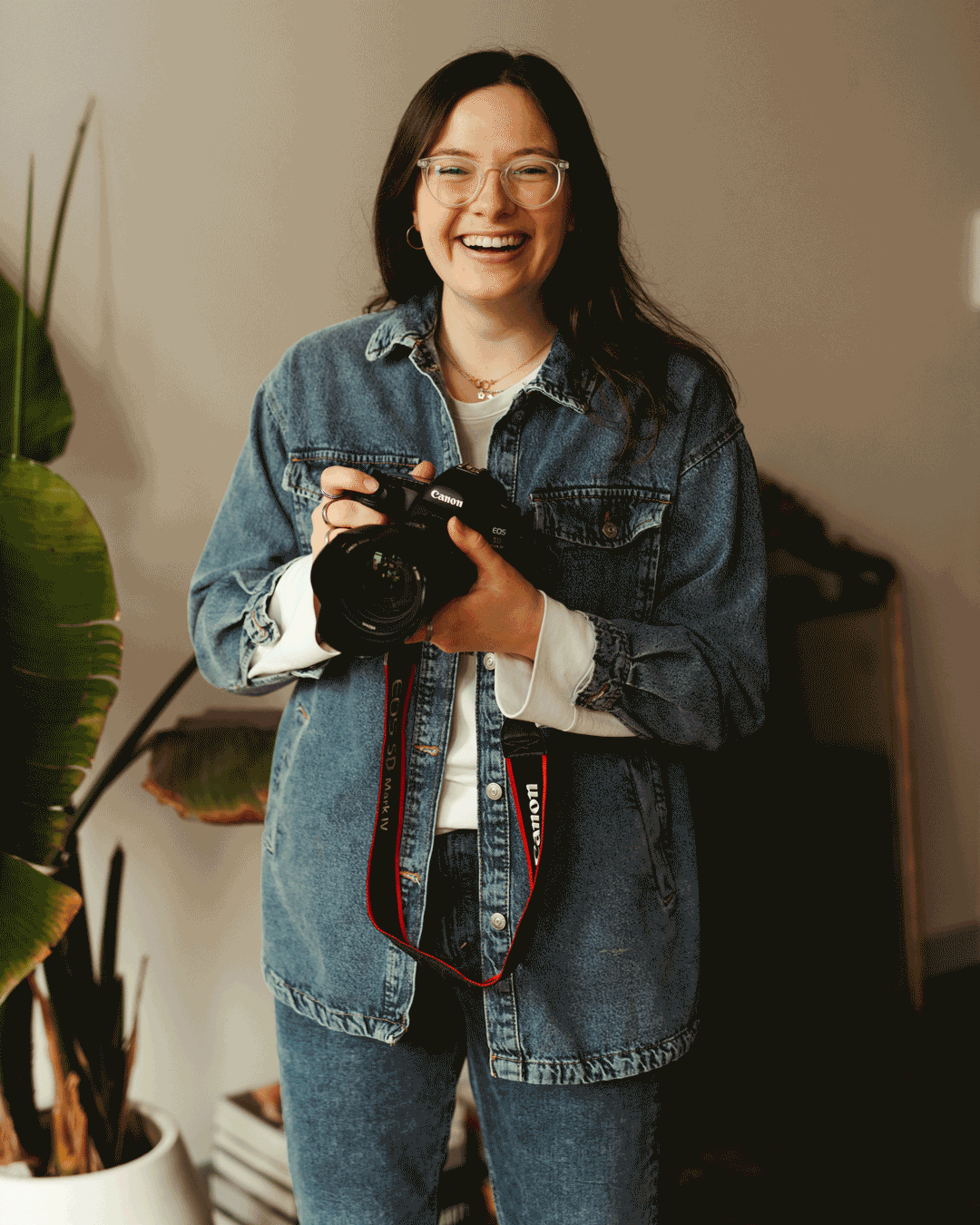woman holding camera while wearing a denim jacket and smiling