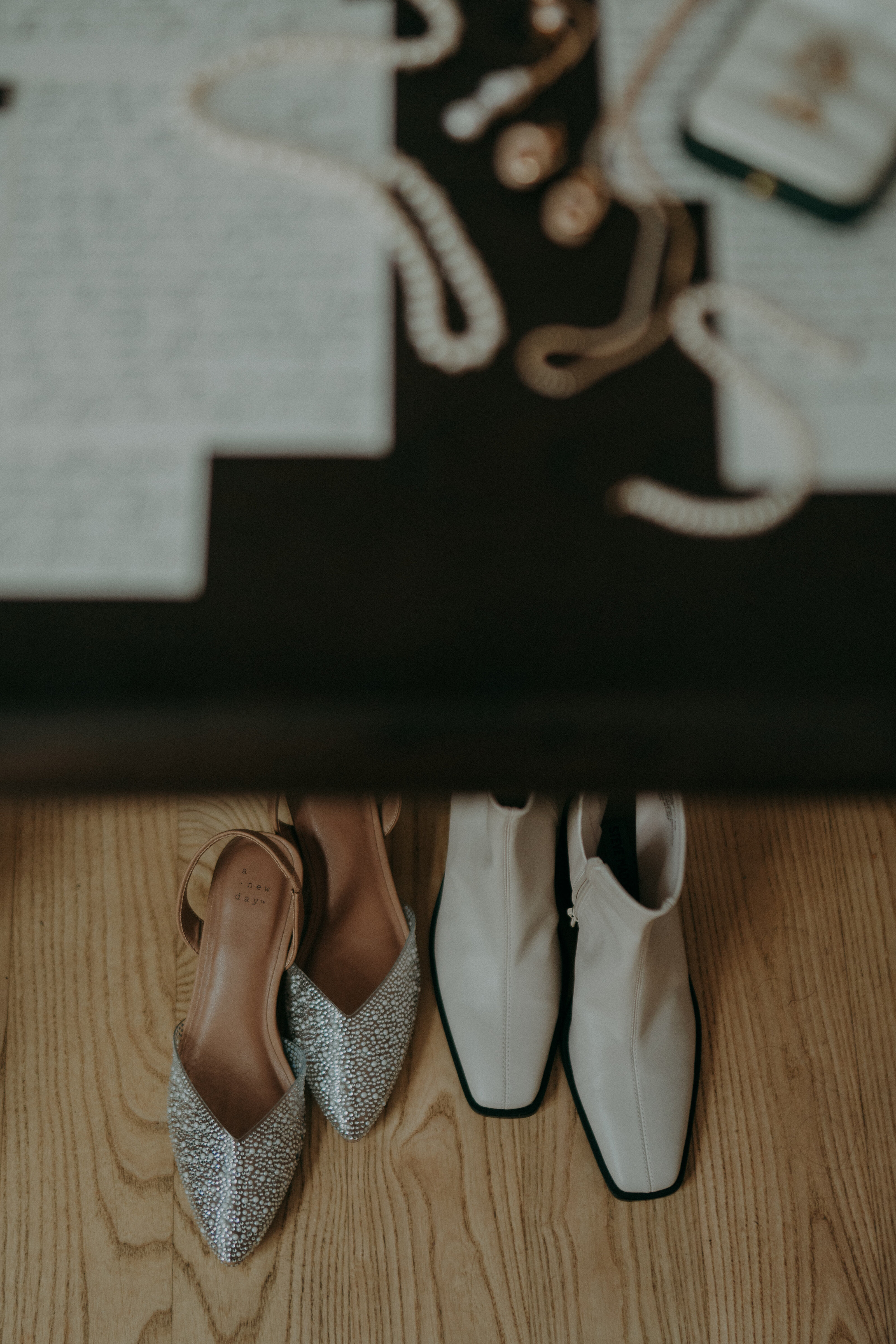 Two pairs of shoes — sparkling heels and white boots — are placed neatly on the floor next to a table with jewelry and notes.