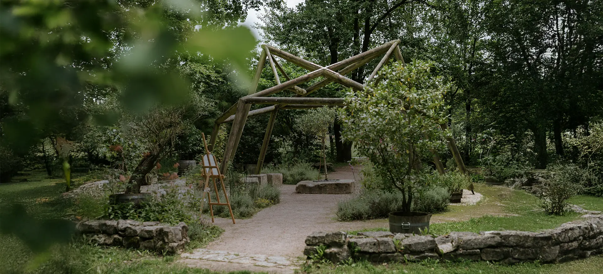 Holzgerüst, Steinbänke und üppiges Blattwerk formen eine ruhige Freitrau-Kulisse im Park. Hochzeitsbilder draußen und kreative Hochzeitsfotografie mit organischer Atmosphäre
