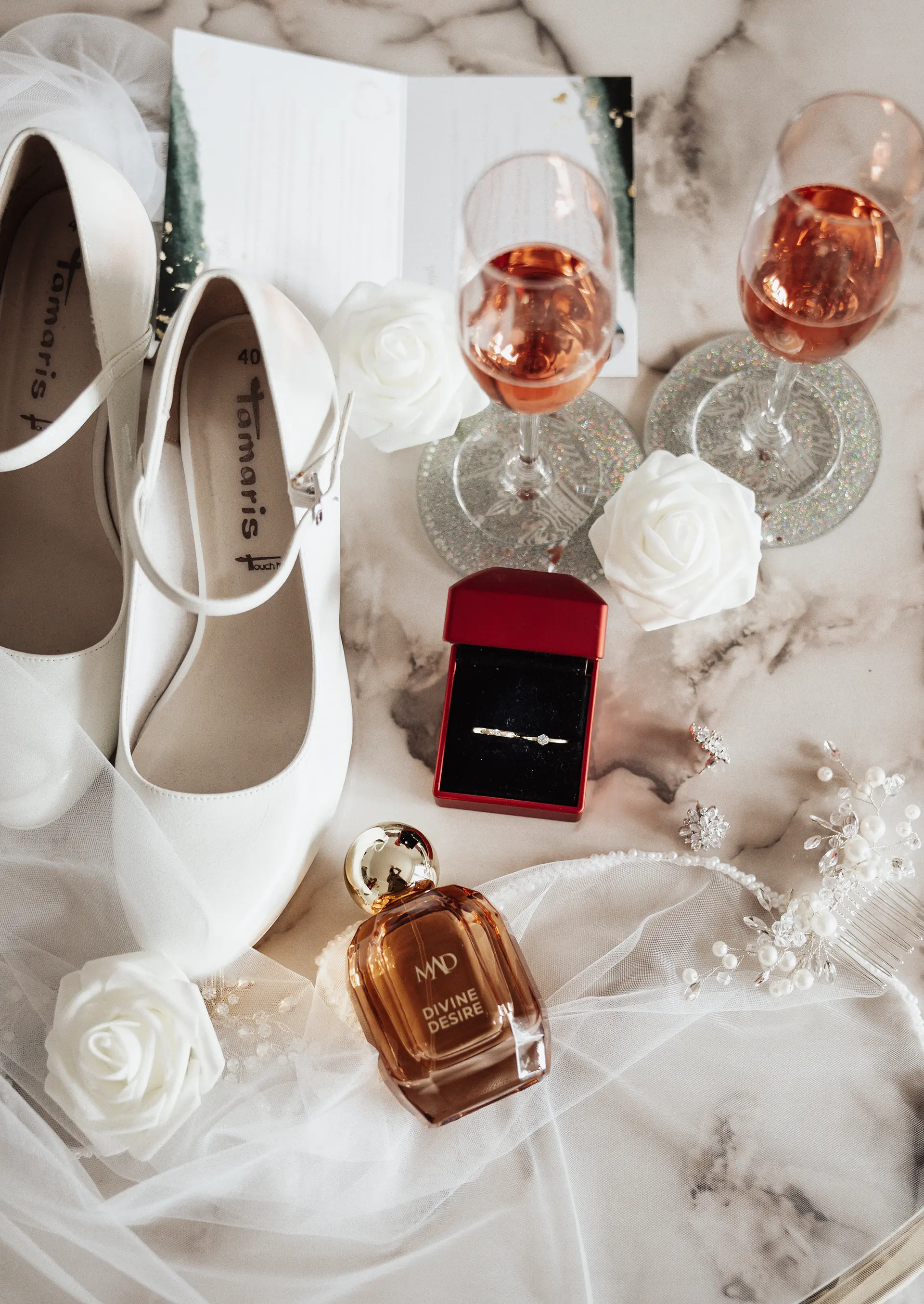 Brautschuhe und Schleier neben Ring im roten Etui, zwei Gläser Rosé, Parfum und Perlenschmuck auf Marmor – edles Setting für getting ready fotografie und natürliche hochzeitsfotografie