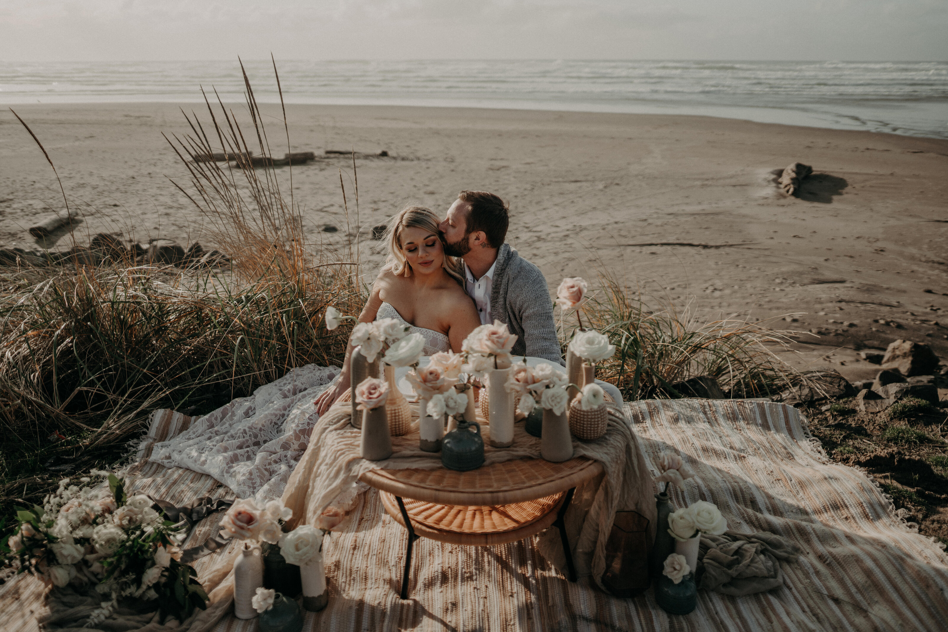 Couple at an intimate elopement table setup on the beach, surrounded by flowers
