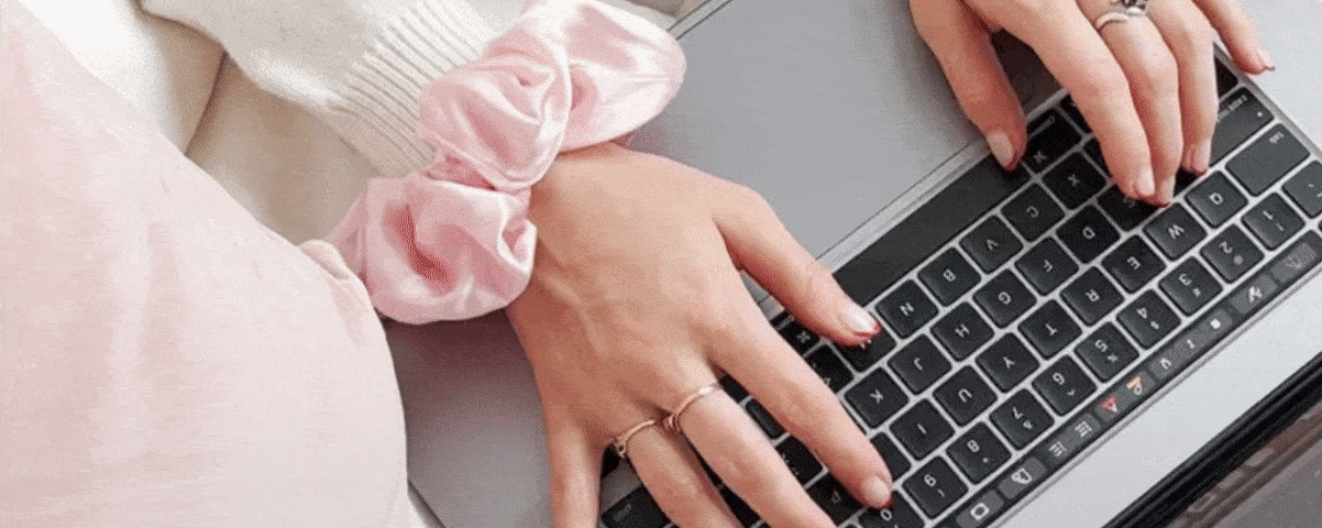 A gif showing two hands  typing on a grey lap top, with a sill pink scrunchie around one of their wirsts.