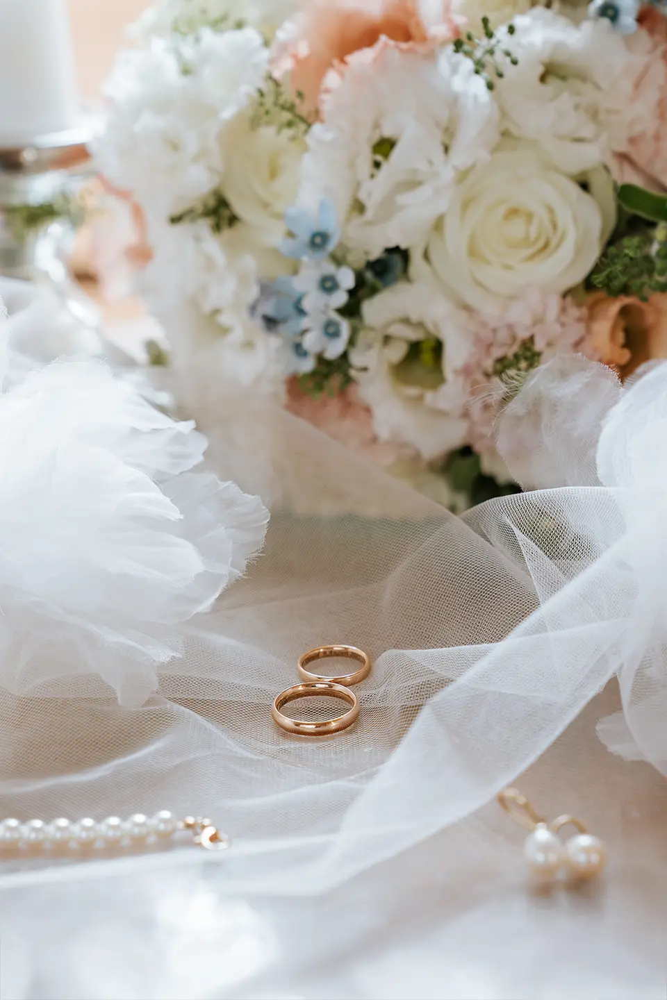 Zwei goldene Ringe ruhen auf weichem Tüll, dahinter ein pastelliges Blumenarrangement. Fine art hochzeitsfotografie verbindet klassische hochzeitsfotos zu zeitlosen Erinnerungen