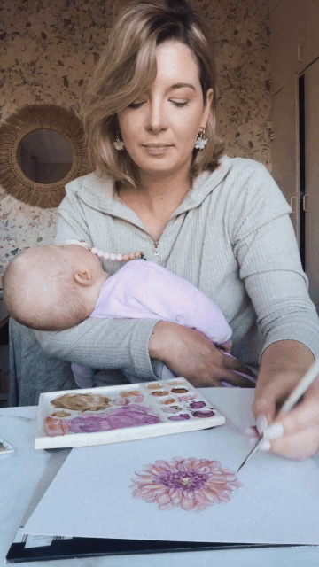 Close-up of Jess Meyer painting watercolour florals while her newborn rests on her lap.