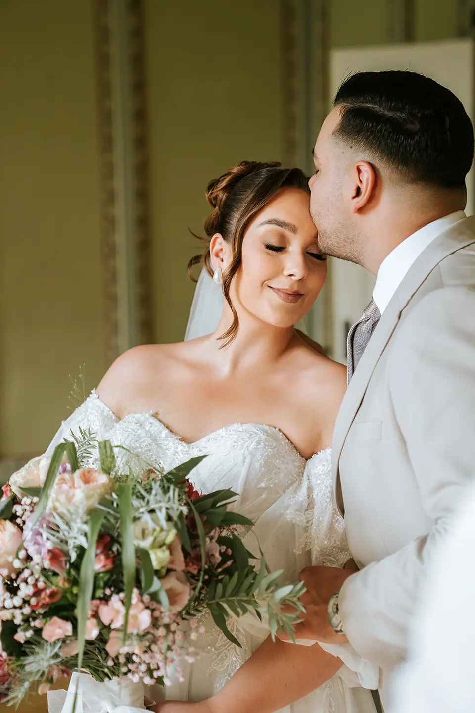Braut mit geschlossenen Augen genießt den Stirnkuss des Bräutigams im Saal; Strauß setzt Akzente – natürliche hochzeitsfotografie, First Look Video Kiel