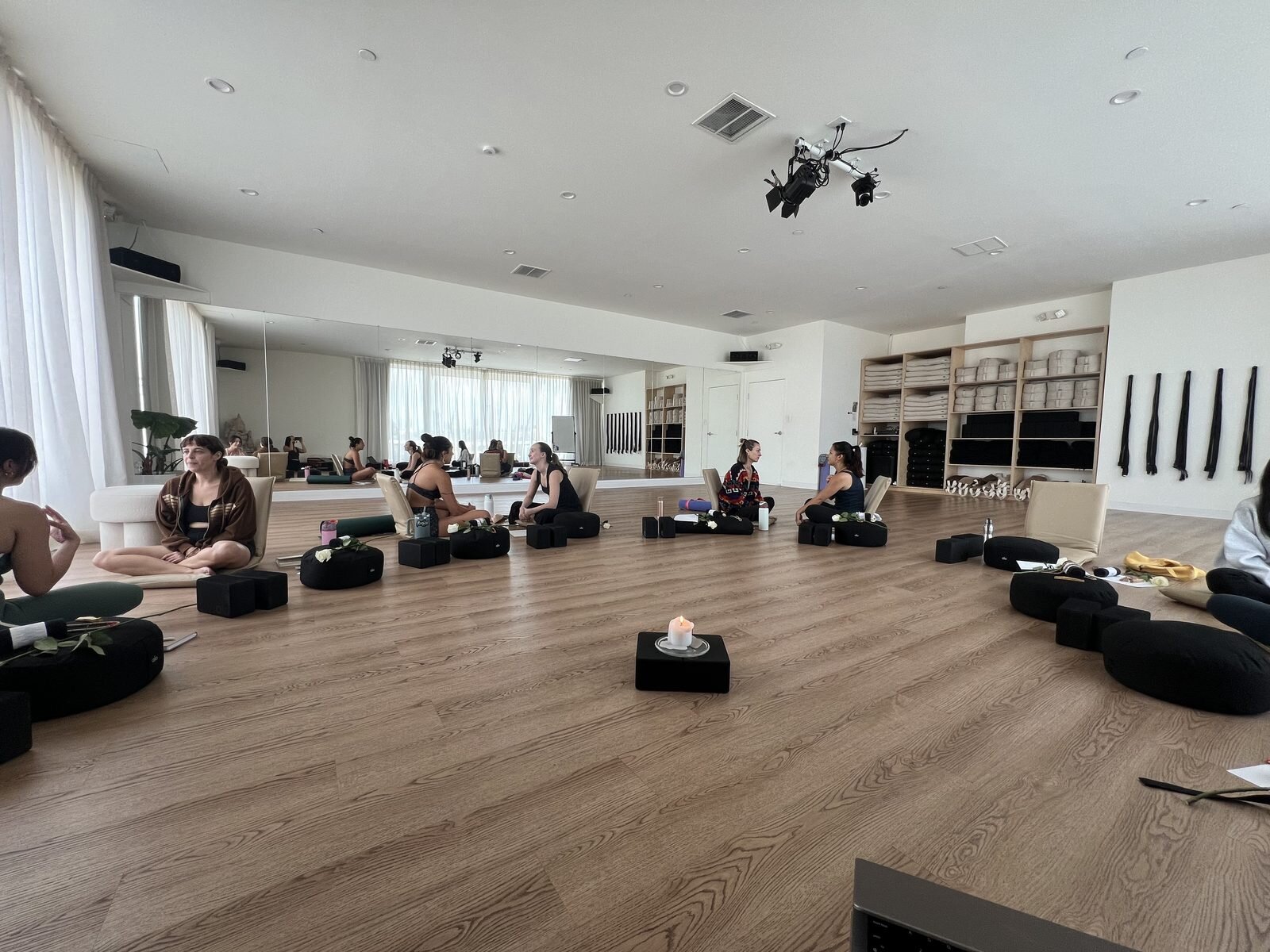 Facilitator trainees seated on black meditation cushions arranged in a wide circle for group discussion in a spacious, naturally lit Ceremny studio.