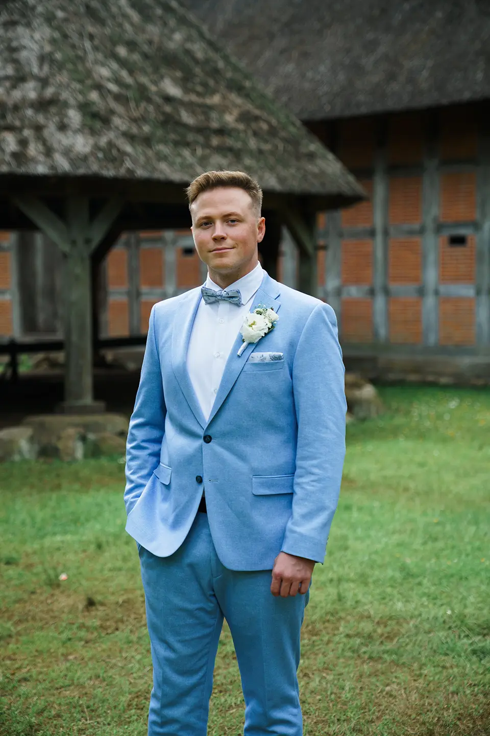 Bräutigam im hellblauen Anzug mit Ansteckblume vor rustikalem Fachwerk; ruhiges Porträt für natürliche hochzeitsfotografie, klassische hochzeitsfotos und professioneller fotograf hochzeit
