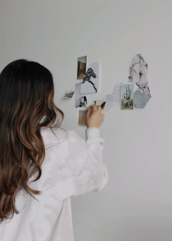 Woman with her back to the camera places an image on a mood board with various images taped to the wall