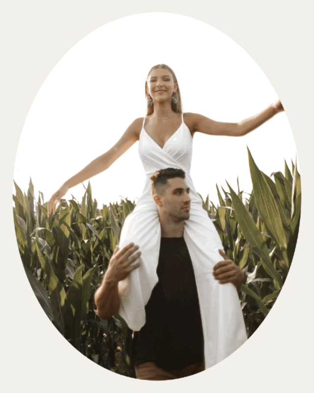 Woman in white jumper sits on man's shoulders as he spins her around in cornfield