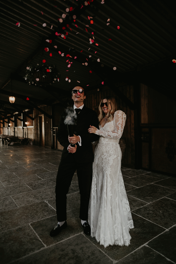 A bride and groom kiss as they are covered in pink and red wedding confetti.
