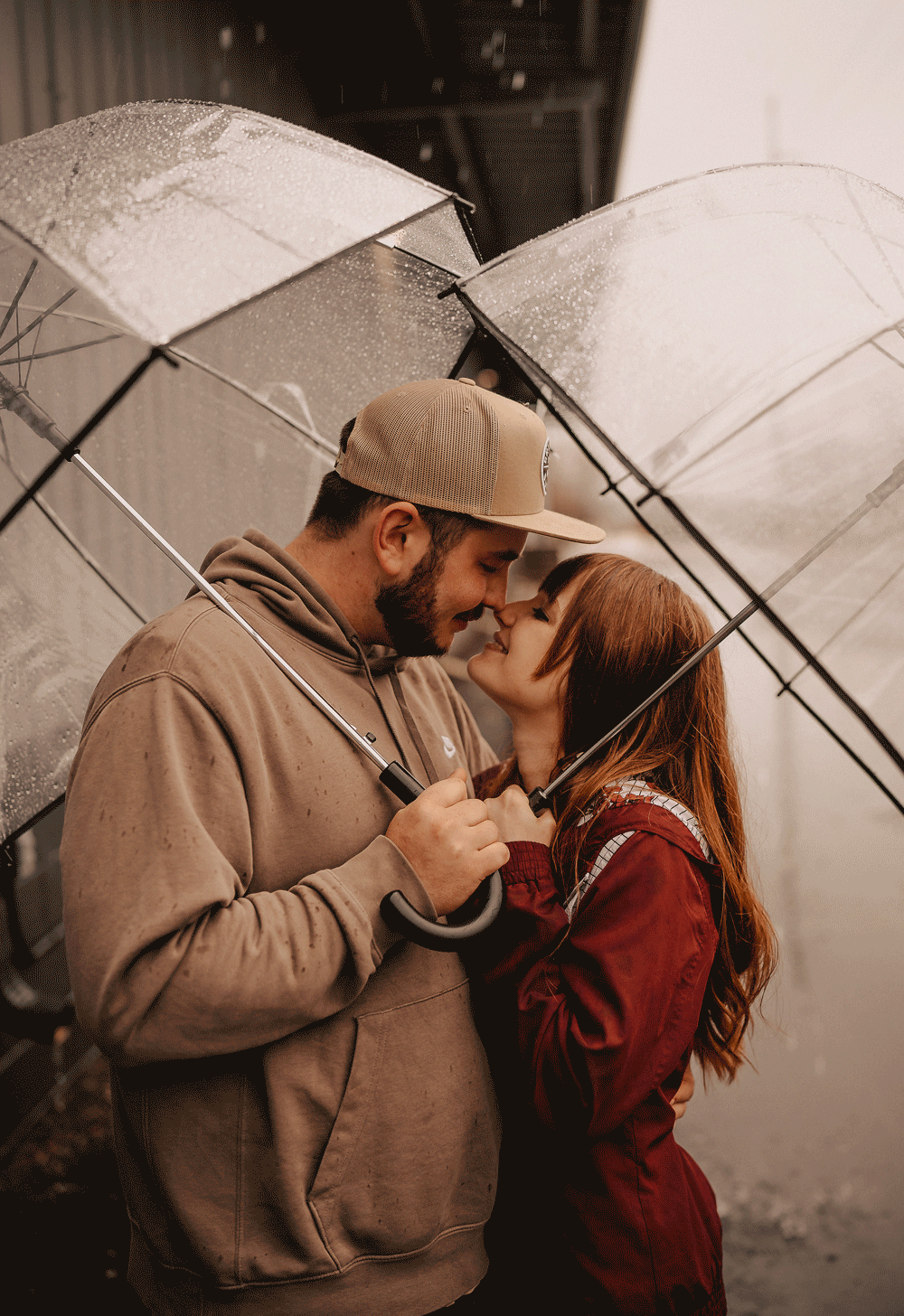 Couple touching noses in the rain with umbrellas for their engagement photos