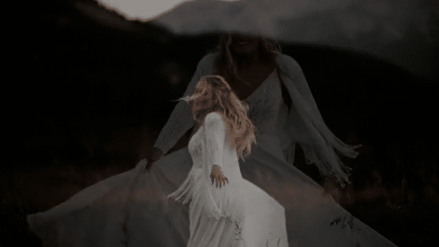 A video of a woman in a white dress and white cardigan spinning around, smiling and moving her dress with her hands.