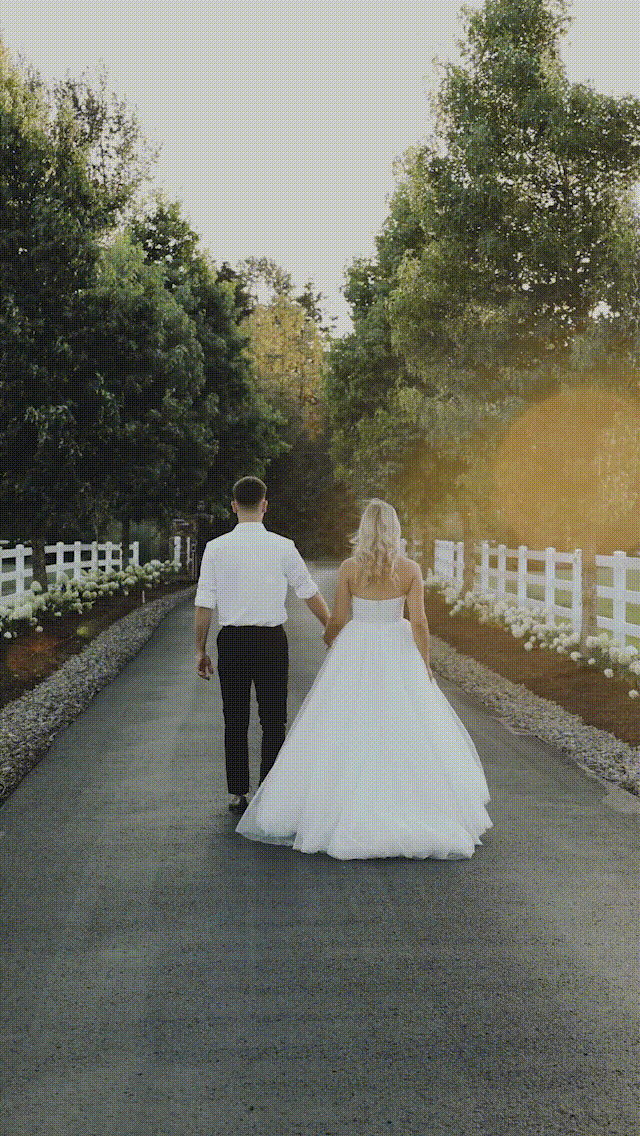 Bride and groom holding hands walk down a tree lined street holding hands