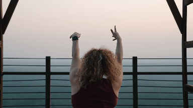 GIF of Alex Paige in front of a sunset stretching her arms up and behind her head