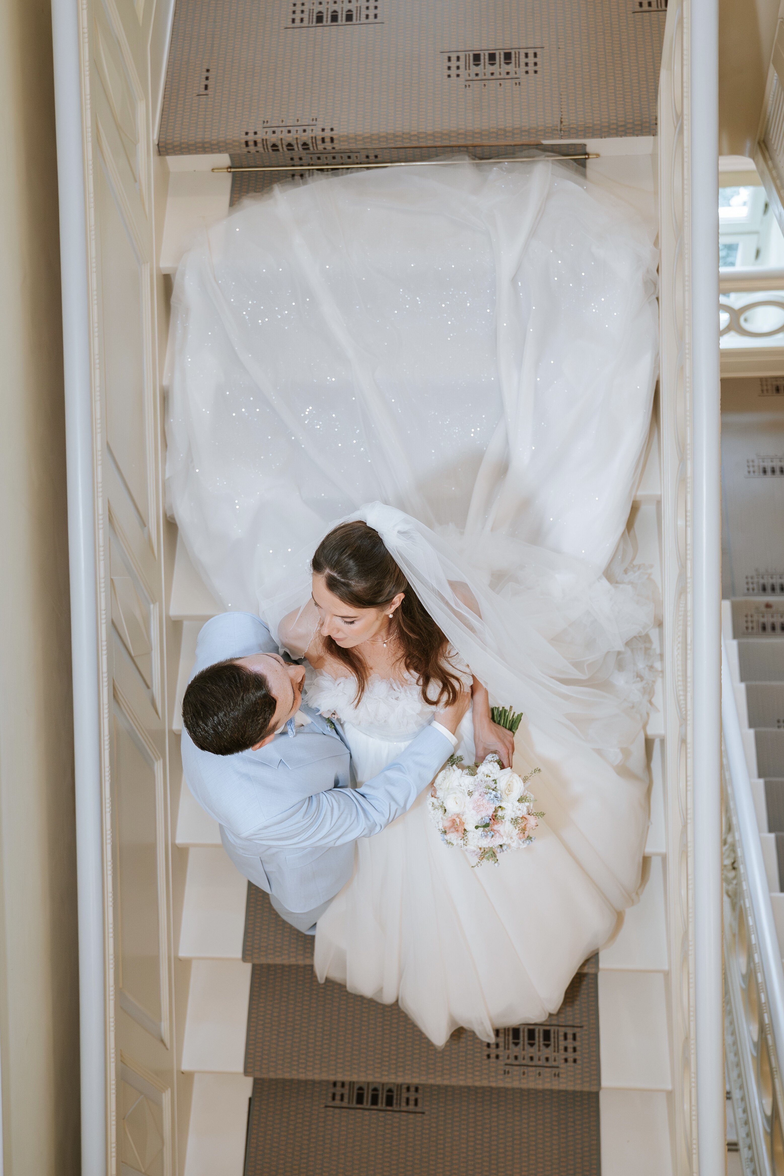 Brautpaar küsst vor gelber Schlossfassade; die Braut hebt den Strauß, Schleier und Schleppe fallen weich – ideal für natürliche hochzeitsfotografie und emotionale hochzeitsbilder