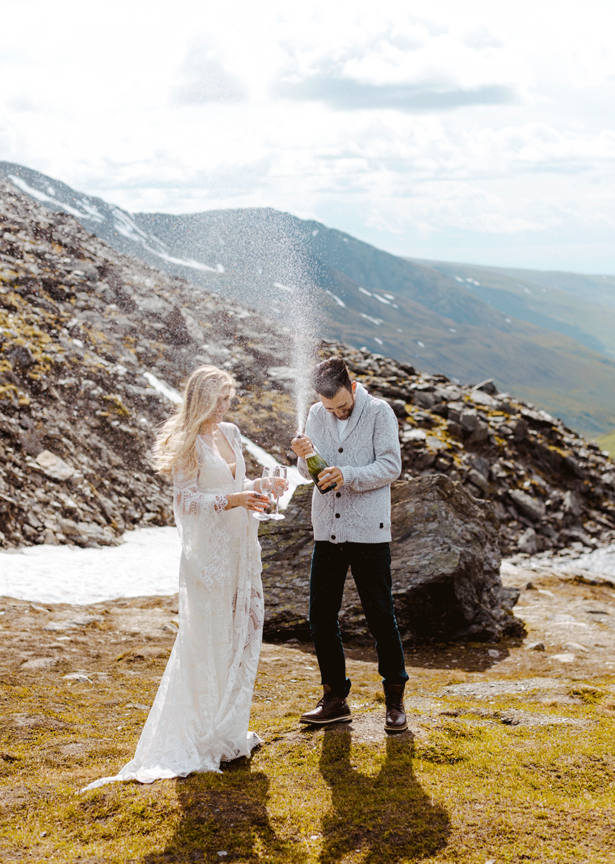 GIF of a bride and groom spraying champagne while kissing in the mountains