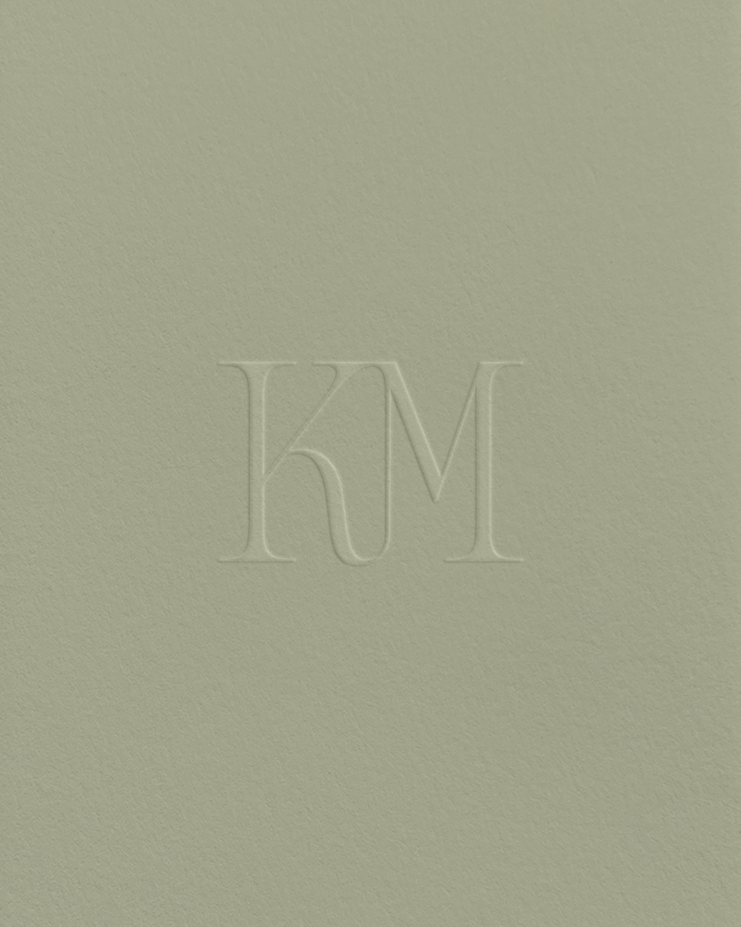 Debossed KM monogram logo for Karen Michelle Photography on textured soft green paper.