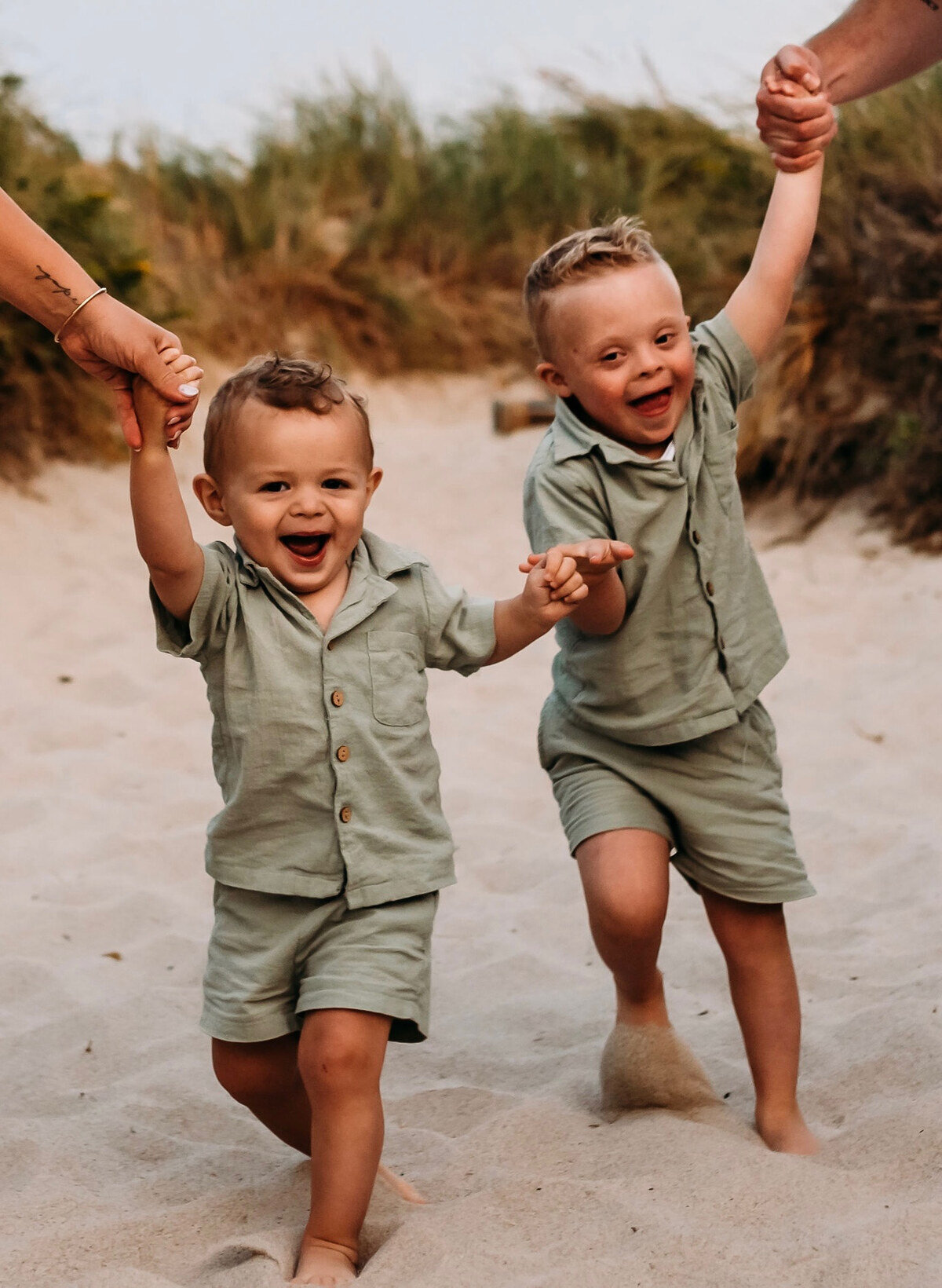 Caleb and Casen Vermeulen laugh as they hold hands on a sandy path.