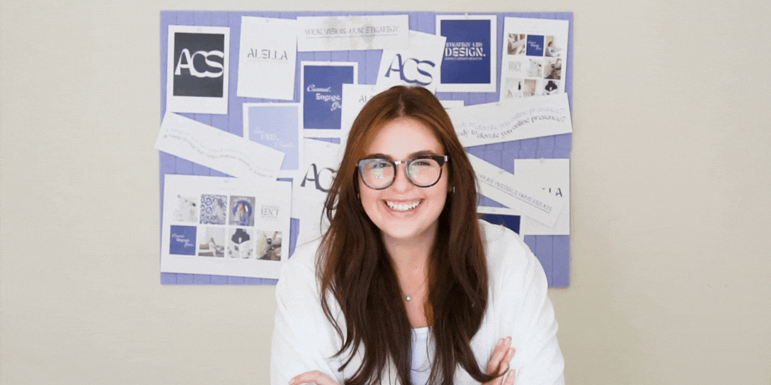 A smiling woman with dark hair and glasses, wearing a white blazer, holding an open silver laptop and looking upwards. She is surrounded by illustrative examples of brand identity designs and abstract shapes, symbolizing the creative partnership and vision a client can achieve by connecting with Alella Creative Studio. 