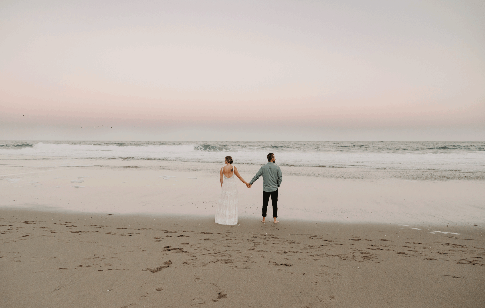 moving GIF of a bride and groom  holding hands as they stare out at the ocean waves