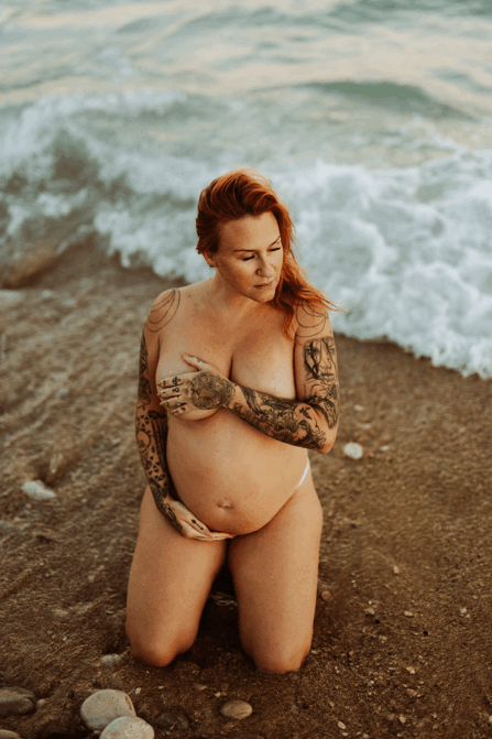 en gravid kvinna sitter i underkläder  på ett fält och känner på sin gravidmage