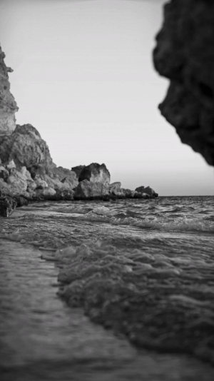 A video of a beach shore in black and white where you can see the waves moving back and forth.