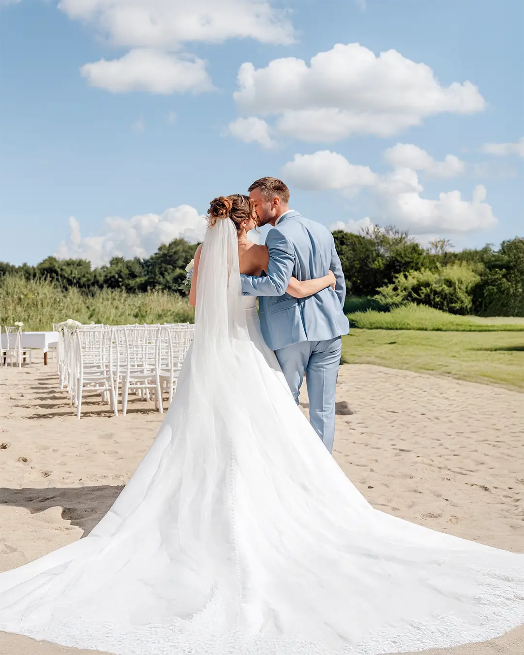 Hochzeitsfotos Schleswig-Holstein – Brautpaar küsst sich bei der Strandhochzeit, mit langer Schleppe im Sand.