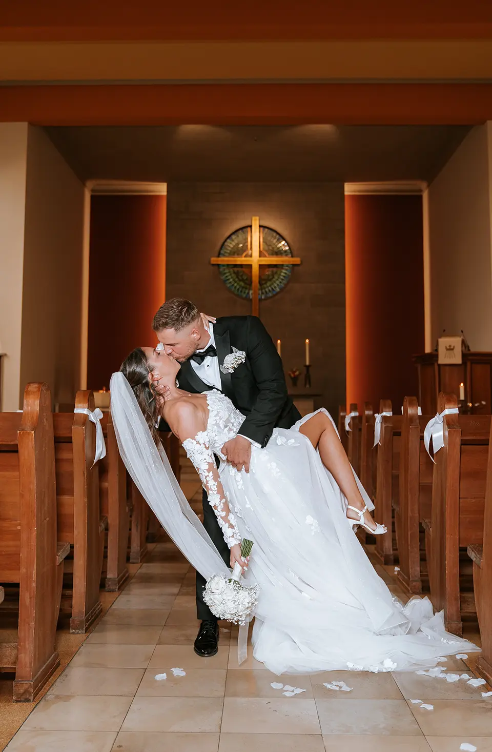 Im Kirchgang neigt der Bräutigam die Braut zum Kuss, Kreuz und Kerzen leuchten; dokumentarischer hochzeitsfotograf erzählt die Feier als klassische hochzeitsfotos