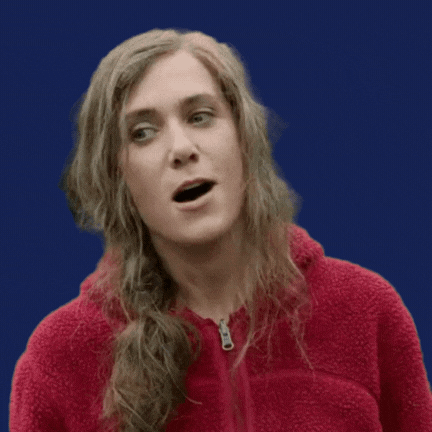 Kristen Wig with disheveled hair and a pilled flannel hoodie saws "wow" with a sarcastic face
