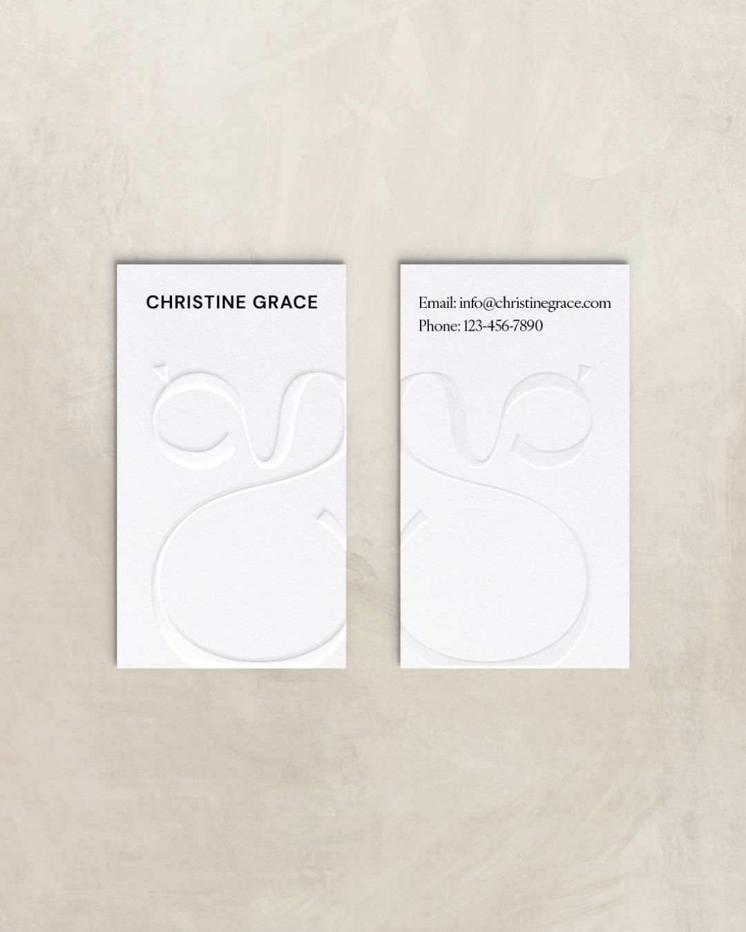 Minimal white business cards embossed with Christine Grace's monogram and contact details, styled on a stone backdrop.
