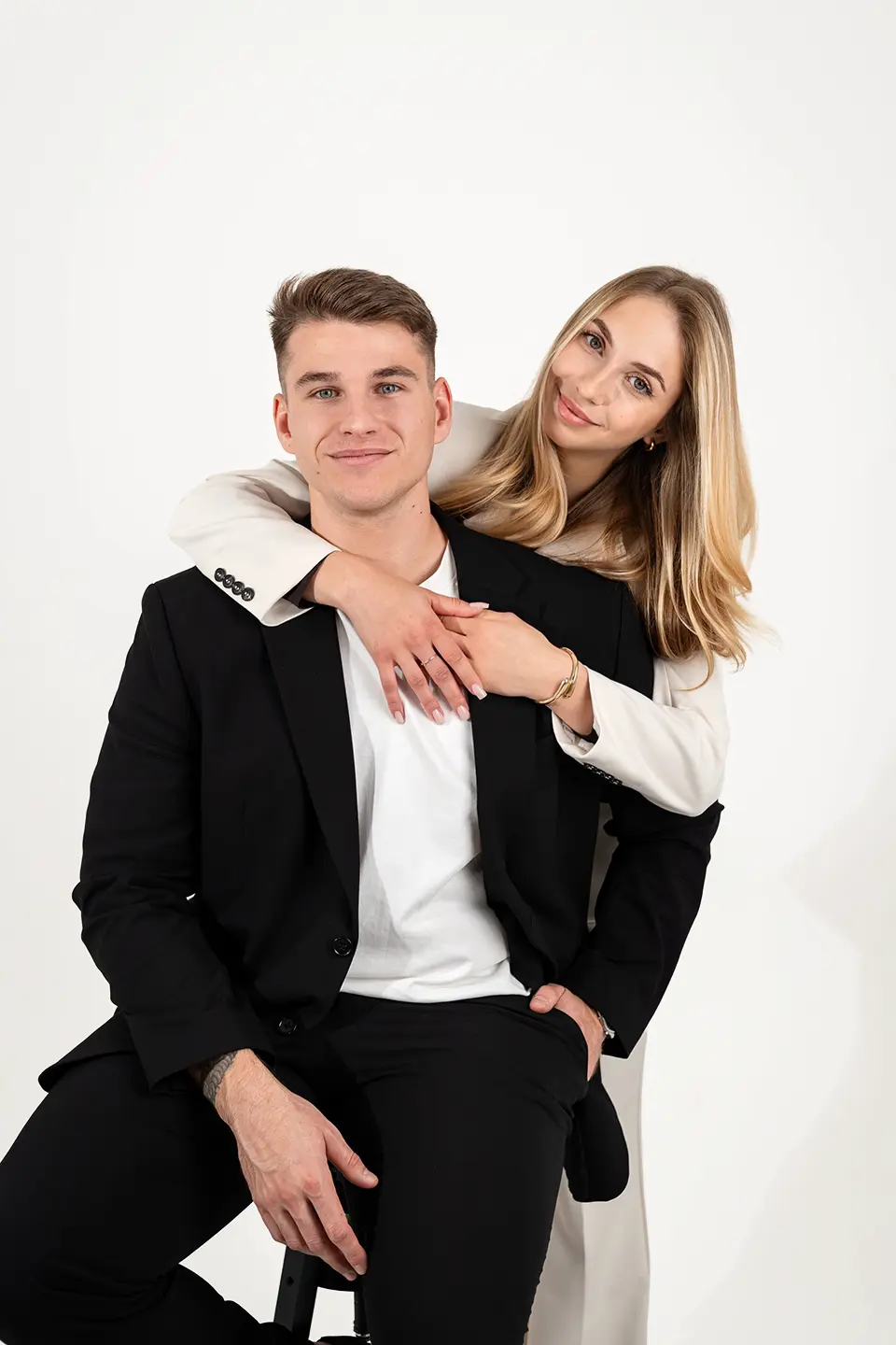 Sie umarmt ihn, er sitzt auf dem Hocker und lächelt. Hochzeitsfotograf mit stil und professionelles Hochzeitsvideo Hamburg – eingespieltes Team