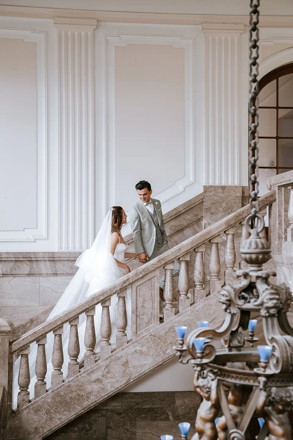 Hand in Hand steigen Braut und Bräutigam die marmorierte Treppe eines eleganten Saals hinauf; klassische hochzeitsfotos, fine art hochzeitsfotografie und hochzeitsfotografie mit stil